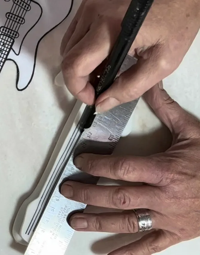 Hand drawing details on a fondant guitar cookie with an edible ink pen.