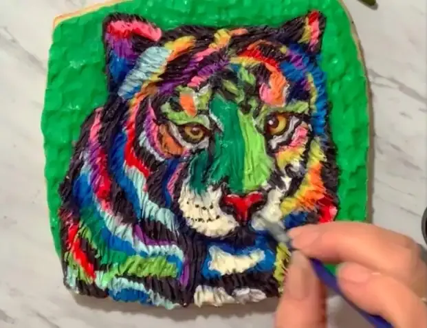 Hand dusting petal dust highlights onto the tiger cookie.
