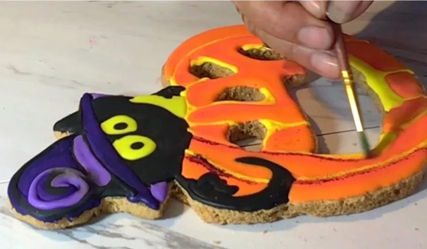 A brush dusts edible powder highlights onto the decorated top cookie.