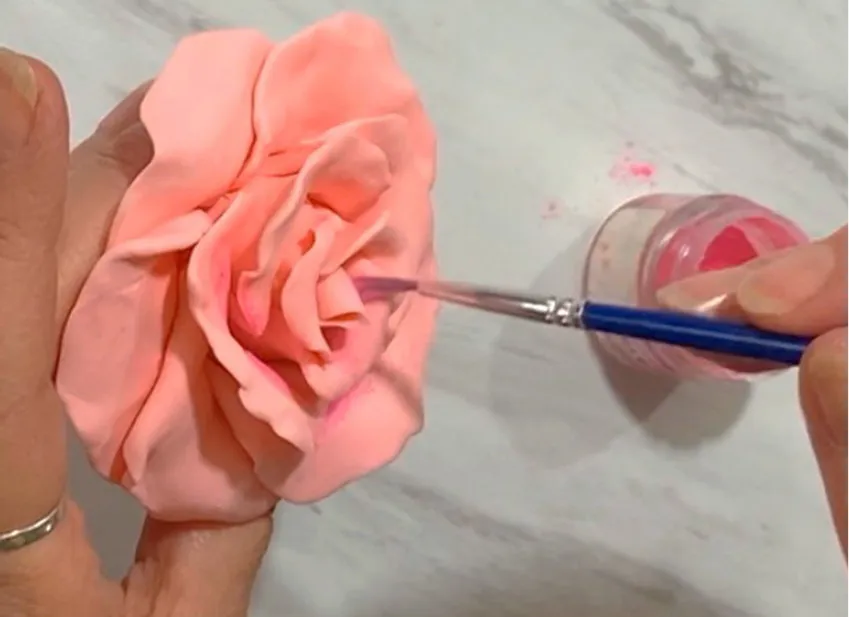 Hand dusting the pink modeling chocolate rose with petal dust using a brush.