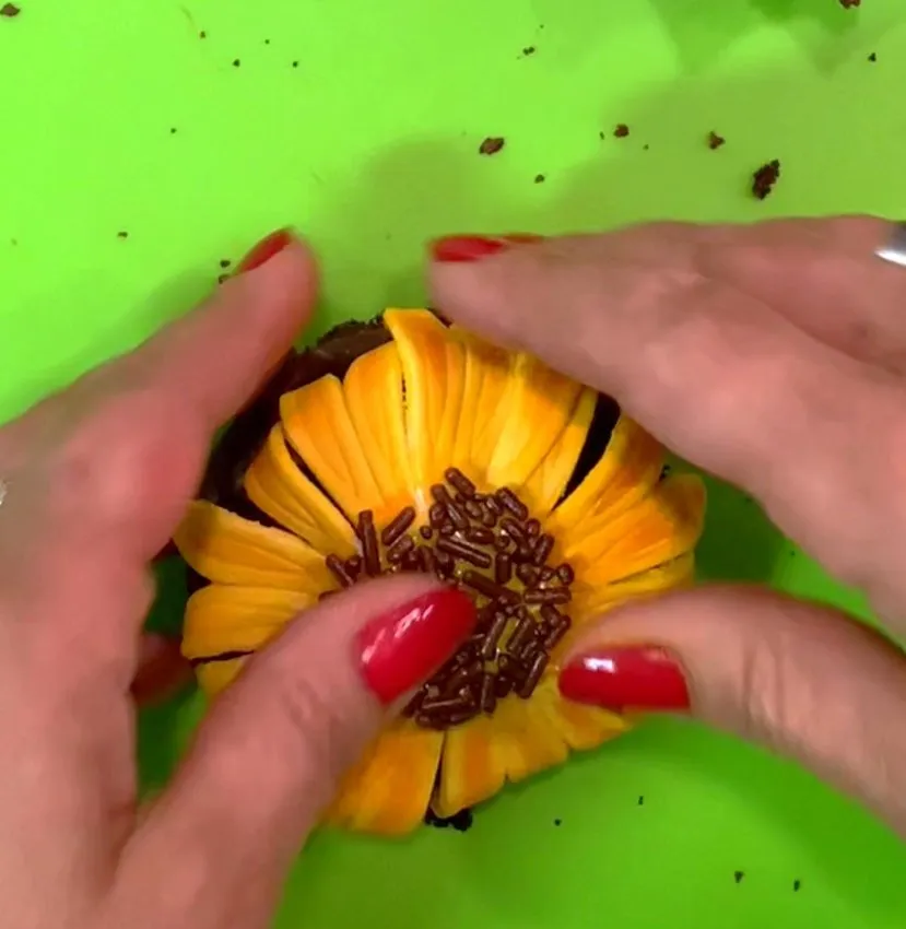 Hands pressing chocolate sprinkles into the center of a gumpaste sunflower.