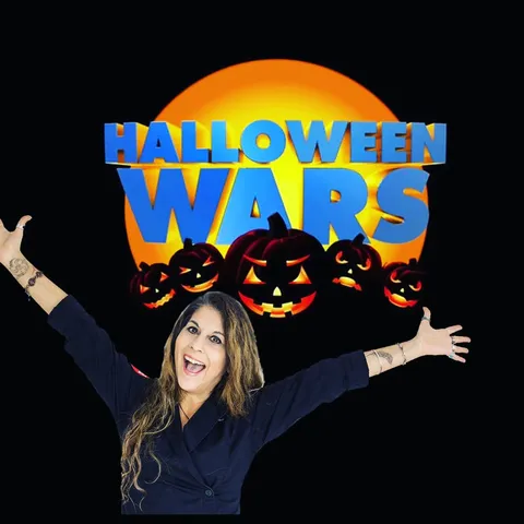 Kim Simons with raised arms in front of a Halloween Wars promotional graphic.