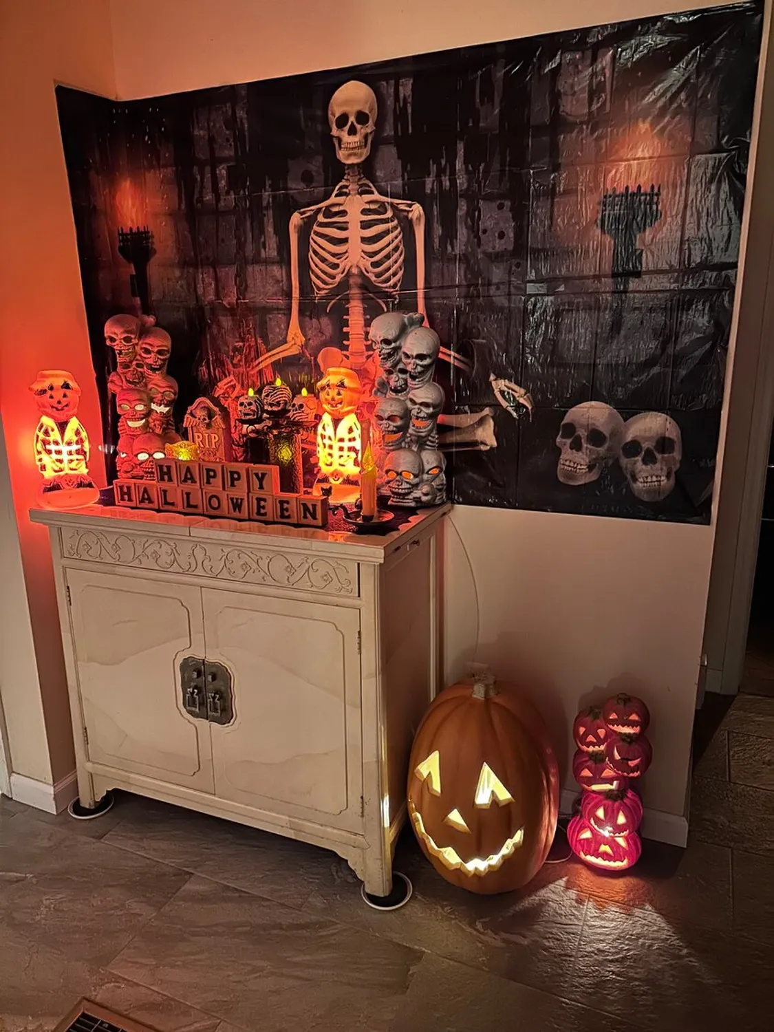 A wall inside a house decorated for Halloween with spooky props including skeletons, tombstones and orange lighting