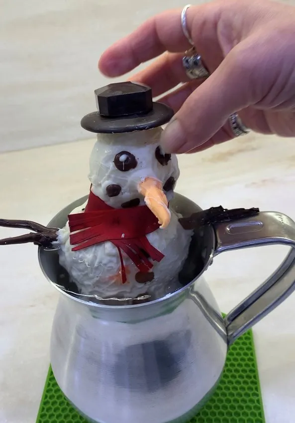 Finished chocolate bomb snowman with hat and scarf in a pitcher.
