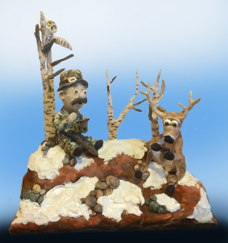 A whimsical sculpted cake diorama depicts a hunter in camouflage sitting on a snowy, rocky base next to a startled reindeer, with an owl perched on a birch tree in the background.