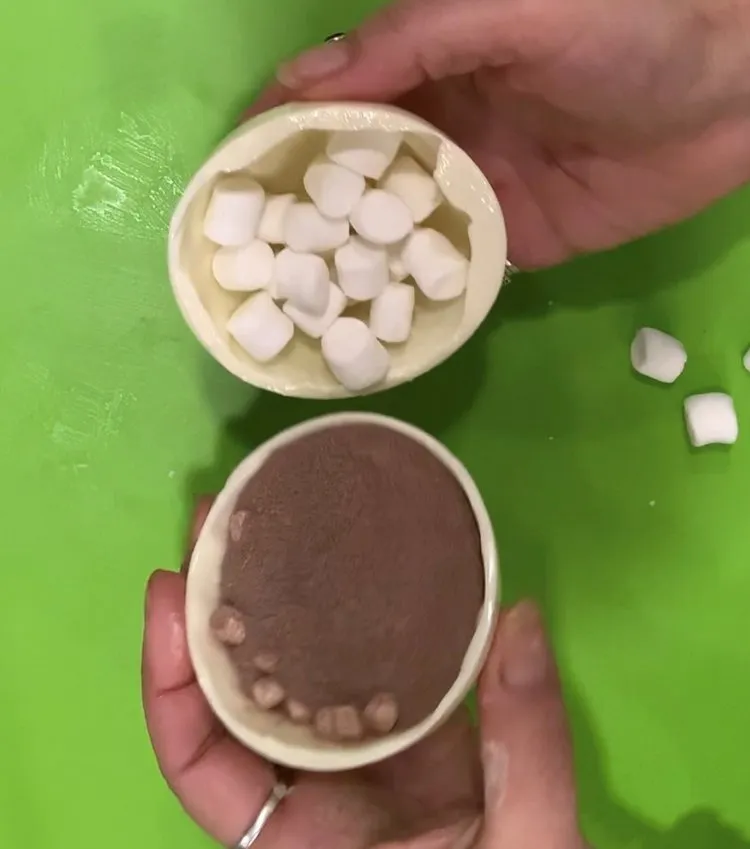 Two chocolate sphere halves showing marshmallows and hot chocolate mix inside.