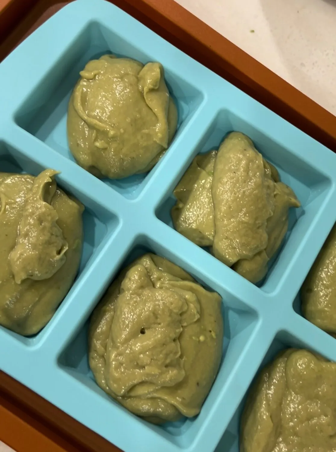 Blended green avocado-banana mixture being placed into molds