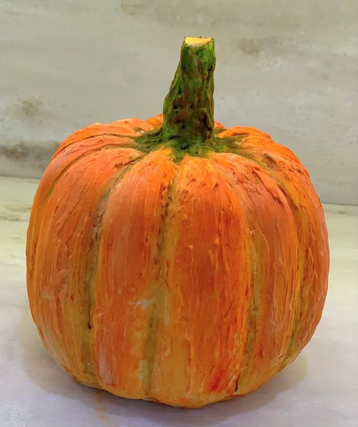 A small round chocolate pumpkin with a green stem on a light surface.