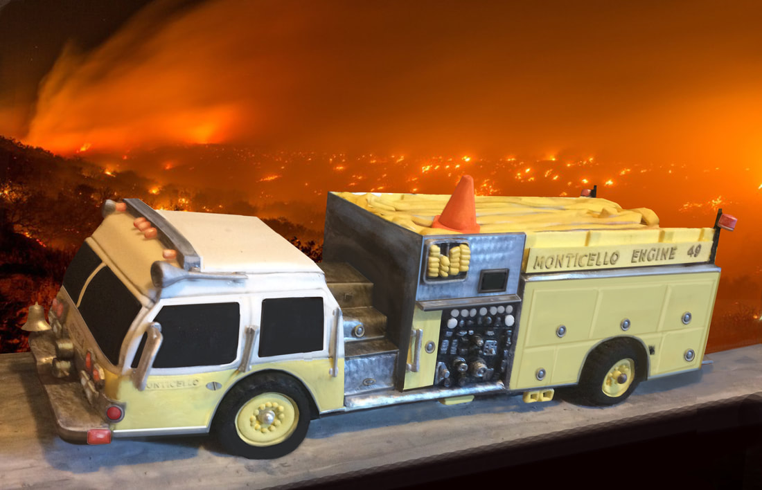A detailed cake sculpted to look like a yellow and white fire engine labeled "Monticello Engine 49," complete with fondant hoses and a cone, set against a dramatic backdrop of a raging wildfire.