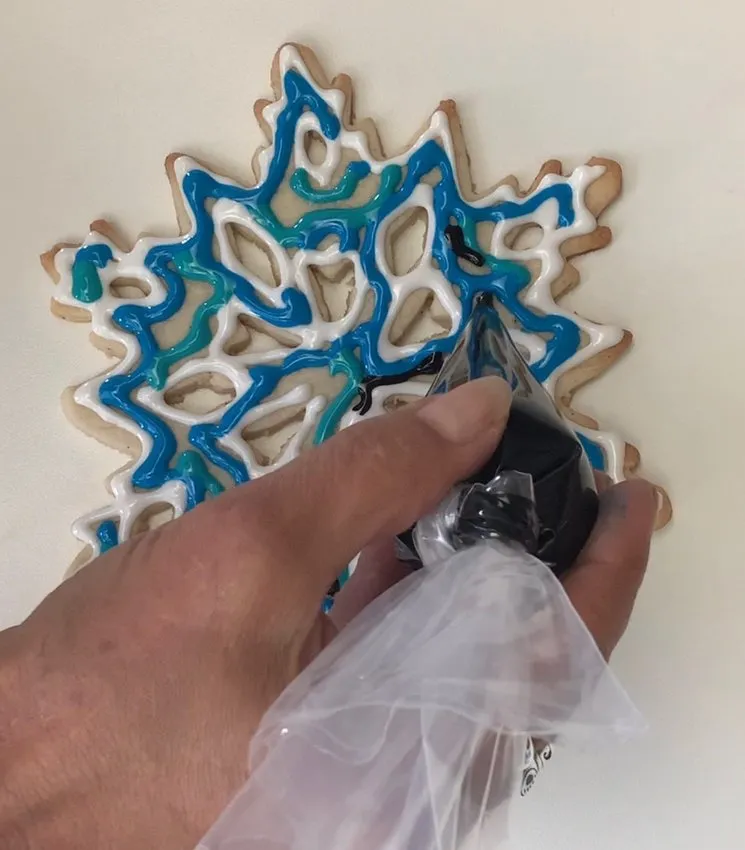 Piping black icing details on a snowflake cookie with blue and white icing