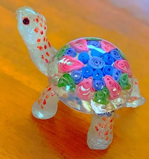Isomalt turtle with colorful floral paper quilling in its shell on a wooden surface.