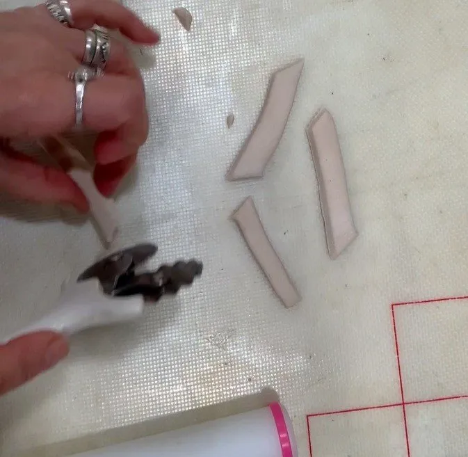 Hands cut beige fondant strips into french fry shapes with a wheel cutter.