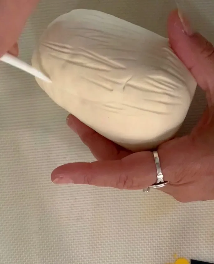 Hand using a cake tool to add fur texture to the fondant bunny body.