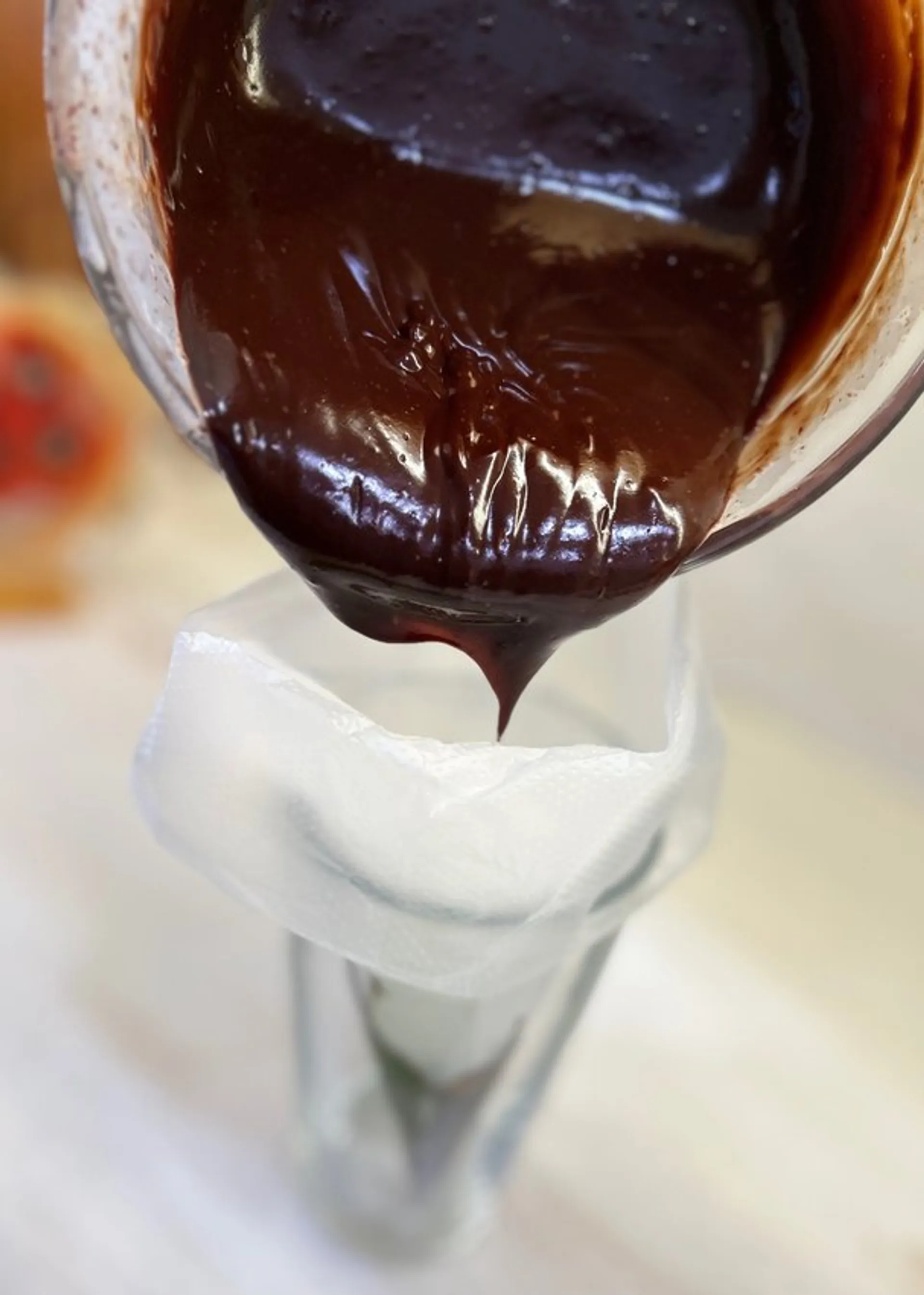 Thick, glossy dark chocolate being poured from a glass bowl into a piping bag fitted with a metal tip