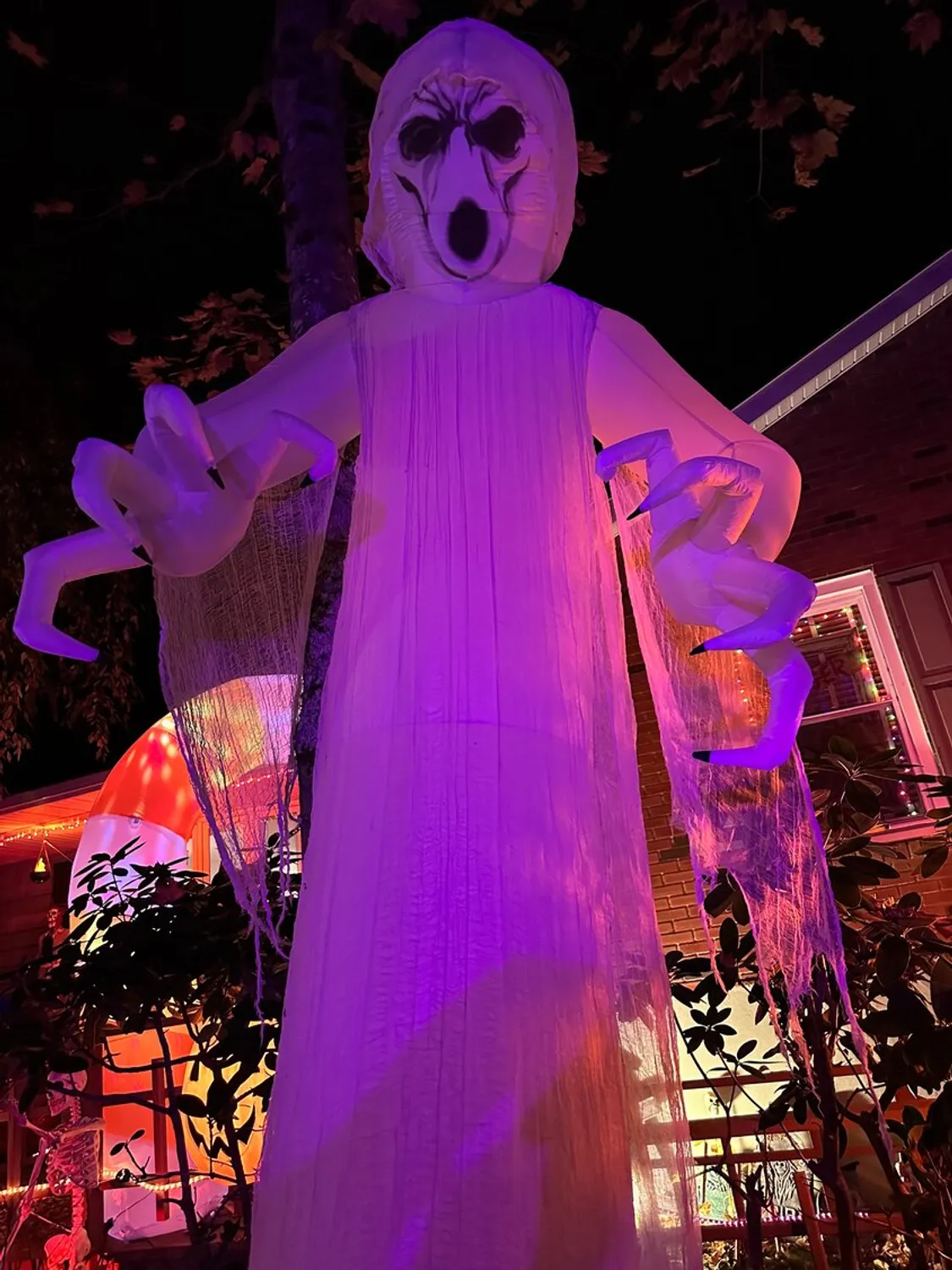 A spooky ghost in the foreground of a house with Halloween decorations