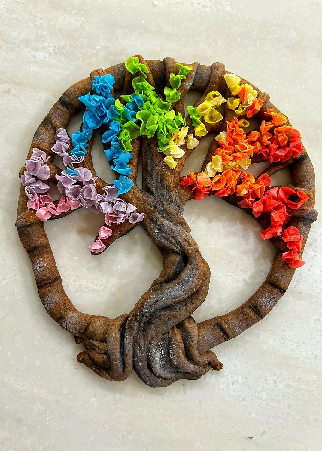 A gingerbread tree of life cookie decorated with colorful frosting leaves in a rainbow gradient
