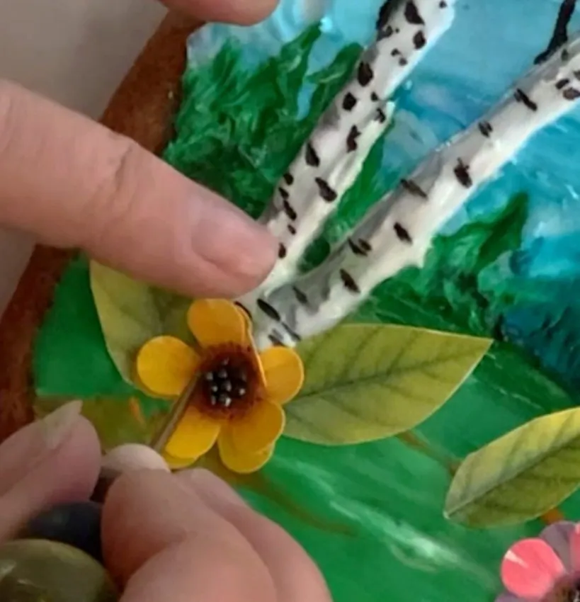 Hand gluing edible paper flowers to the cookie foreground.
