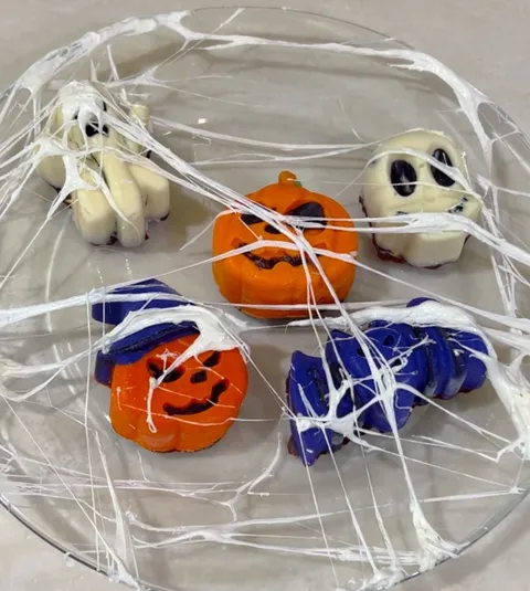 An assortment of halloween-themed treats in glass covered with edible spiderwebs