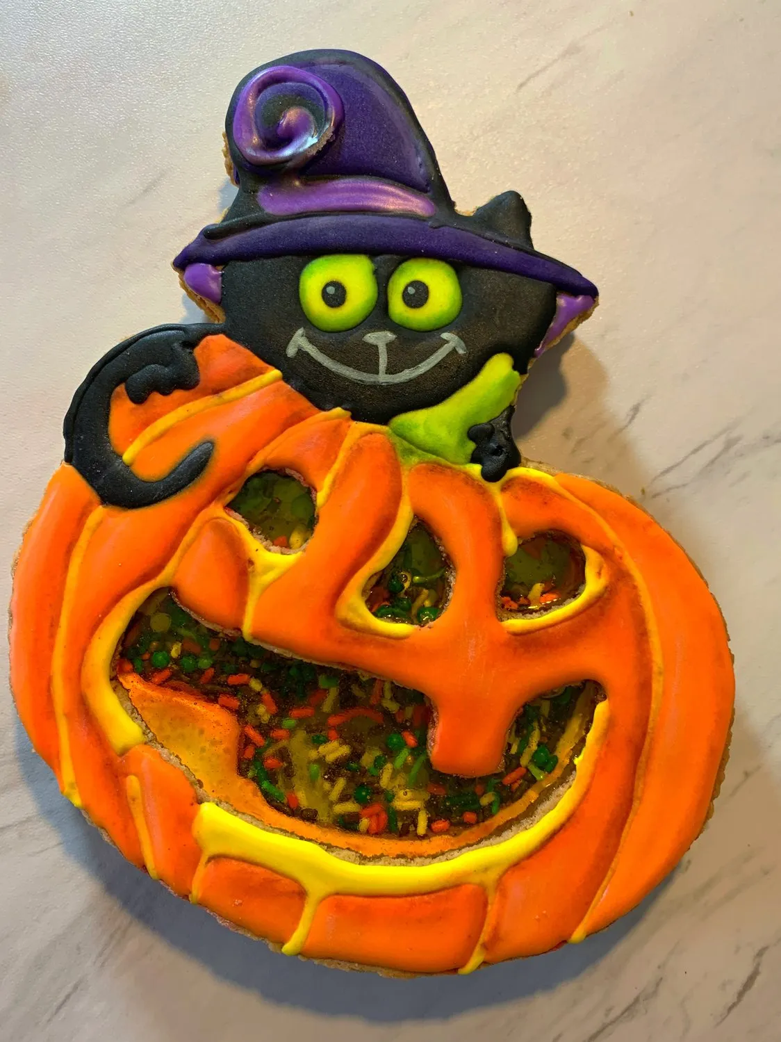 A Halloween shaker cookie decorated as a black cat on a jack-o'-lantern with sprinkles inside