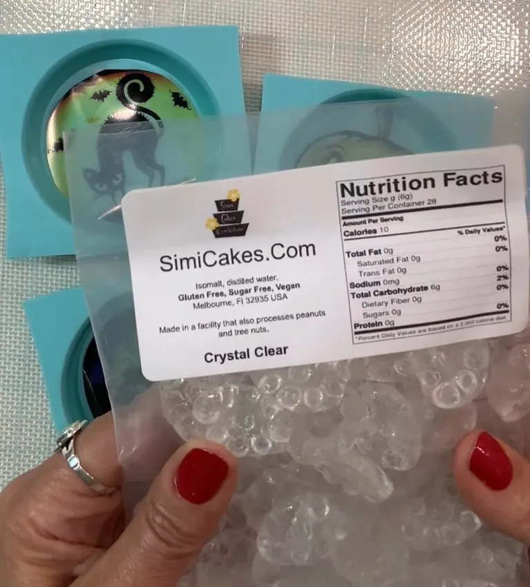 A hand holds a bag of clear isomalt crystals beside silicone lollipop molds.