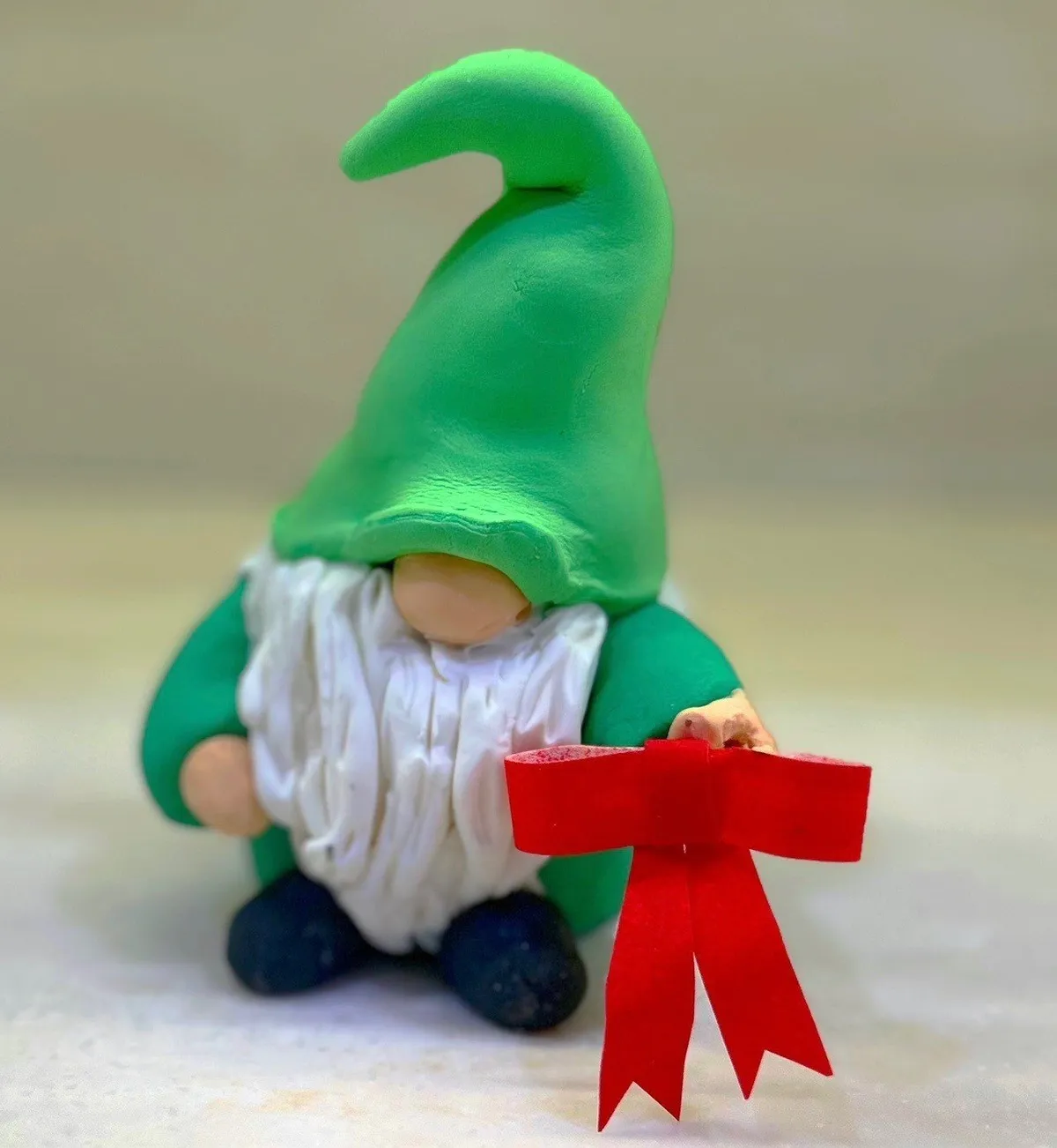 A red fondant gnome with a white beard and green hat holding a holiday ribbon