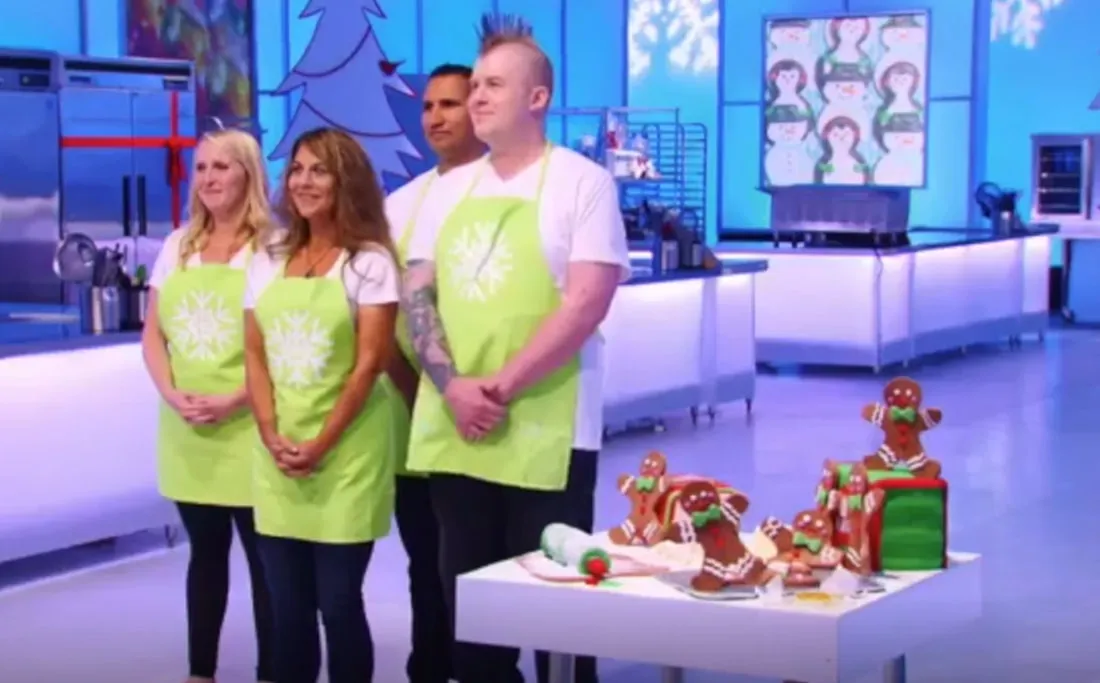 Contestants in lime green aprons next to a gingerbread house display.