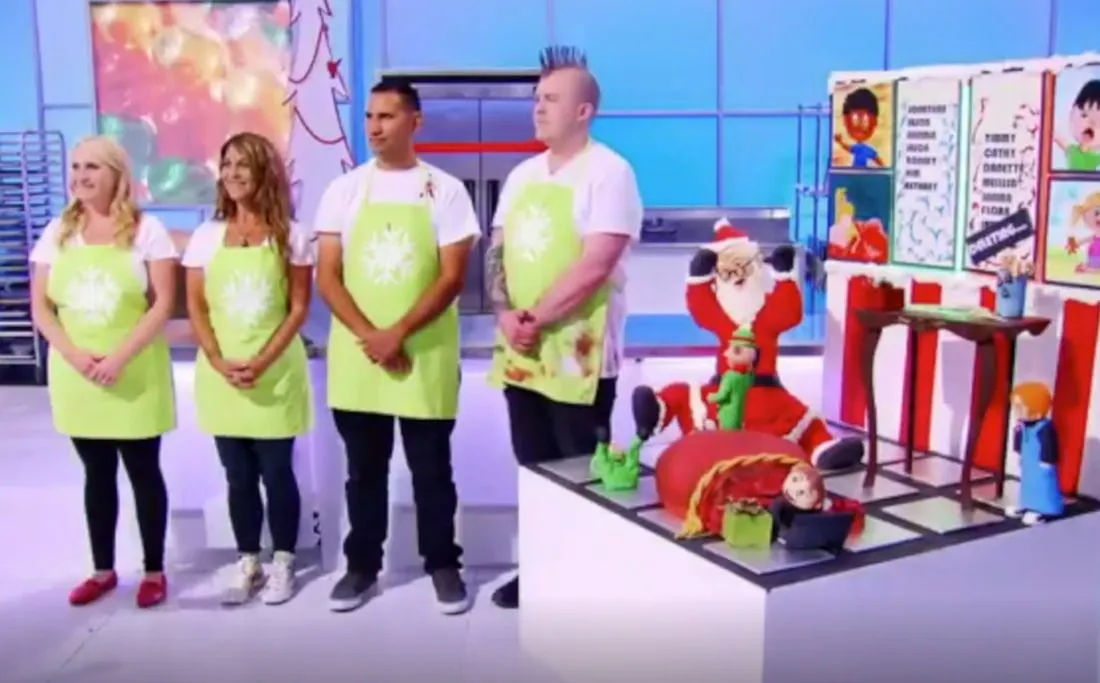 Contestants in lime green aprons next to an elaborate Christmas cake display on Holiday Wars.