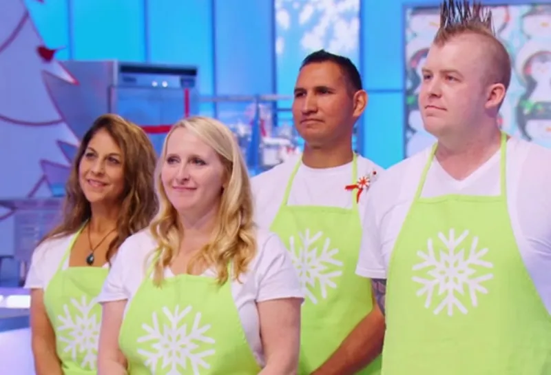 Four contestants in lime green aprons in the Holiday Wars studio kitchen.