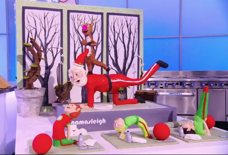 Yoga Santa cake display with a reindeer and elf figures on Holiday Wars.