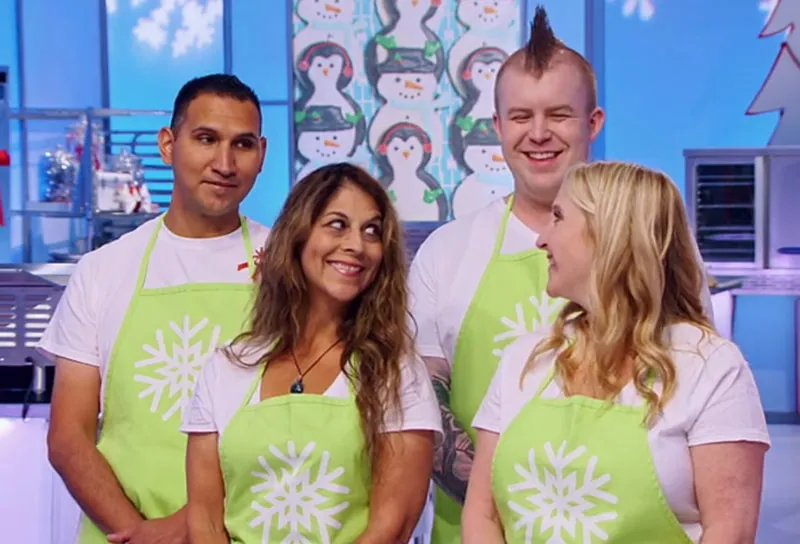 Four contestants in lime green aprons in a winter-themed kitchen studio.