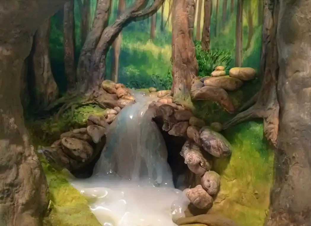 A sculpted cake with a cascading waterfall flowing into a pool, framed by tree trunks and mossy rocks.