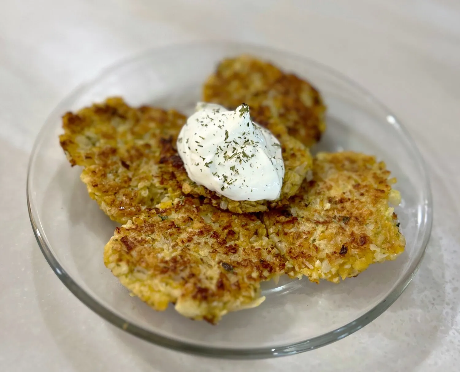 Golden brown cauliflower latkes on a white plate, garnished with sour cream and fresh chives