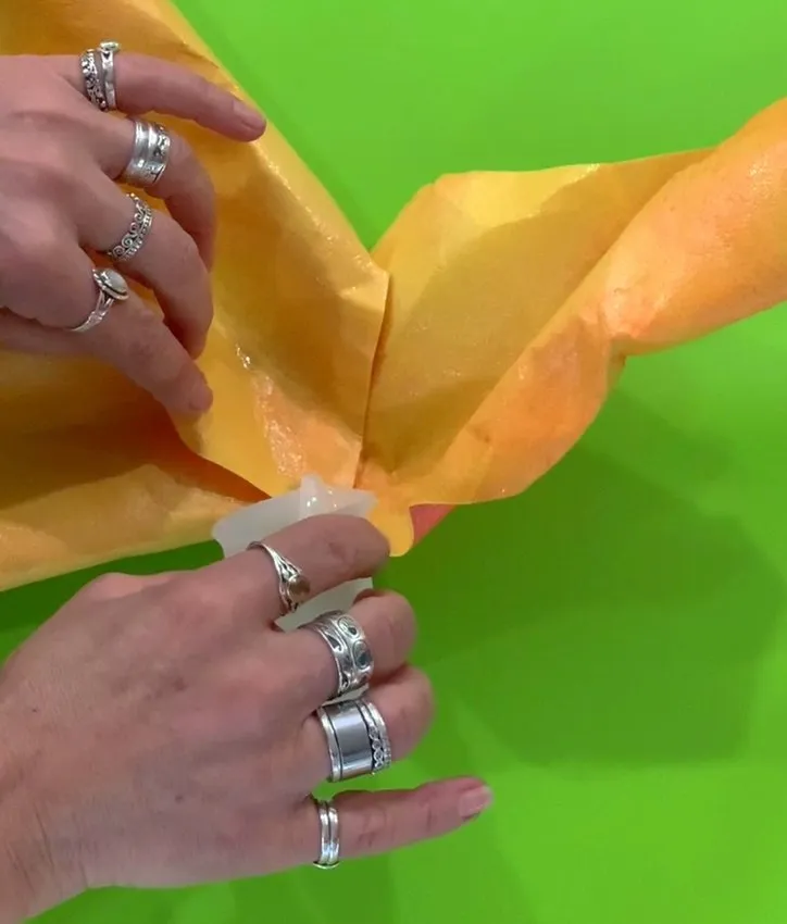 Hands arranging crinkled orange wafer paper petals on a surface.