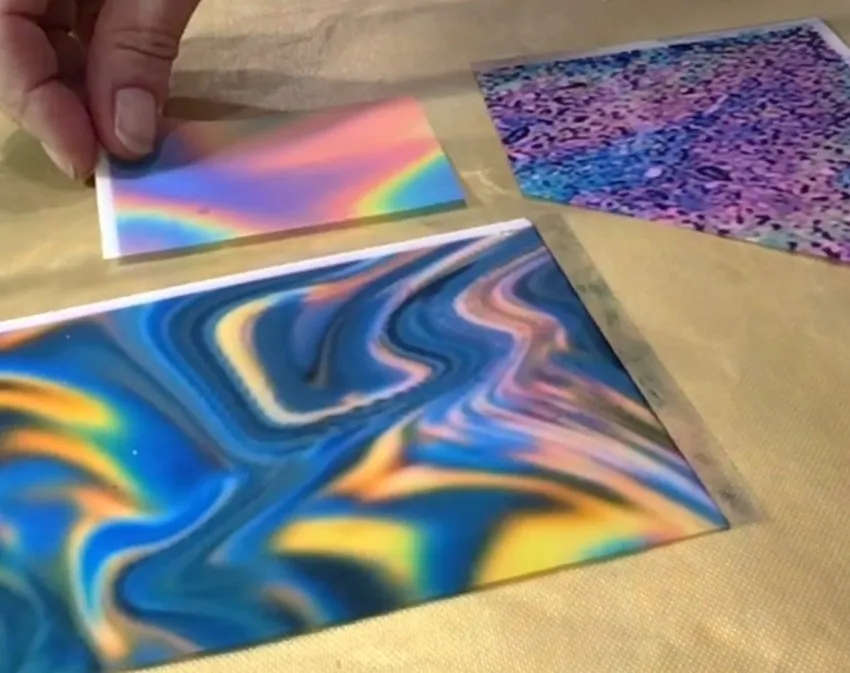 Hand holding a rainbow gradient transfer sheet above other colorful transfer sheets.