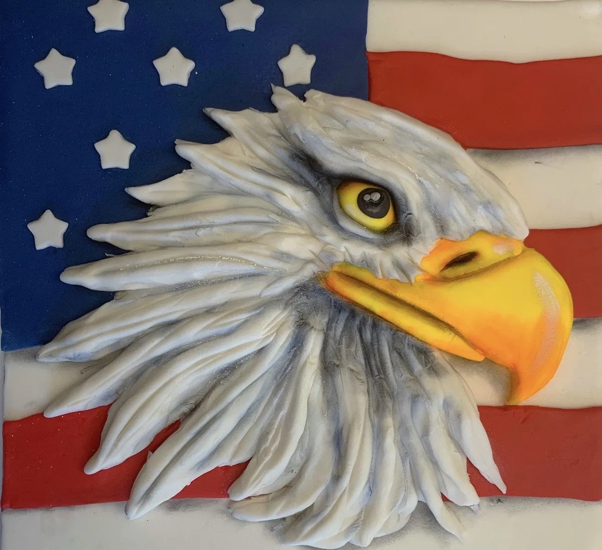 A sculpted bald eagle head made from fondant with feather details and an American flag background