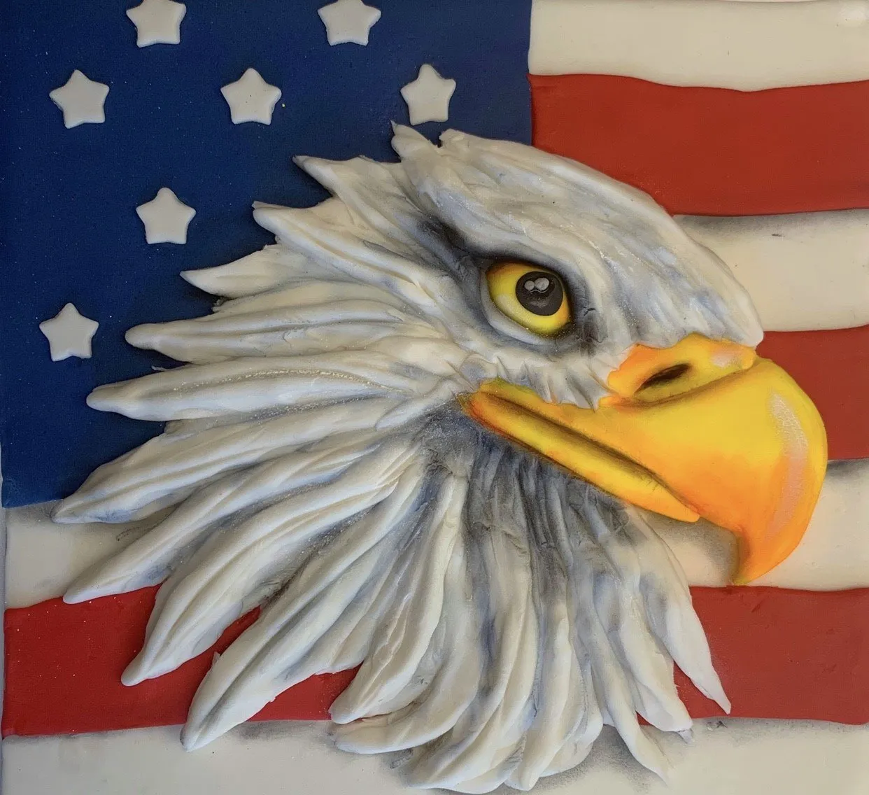 A sculpted bald eagle head made from fondant with feather details and an American flag background