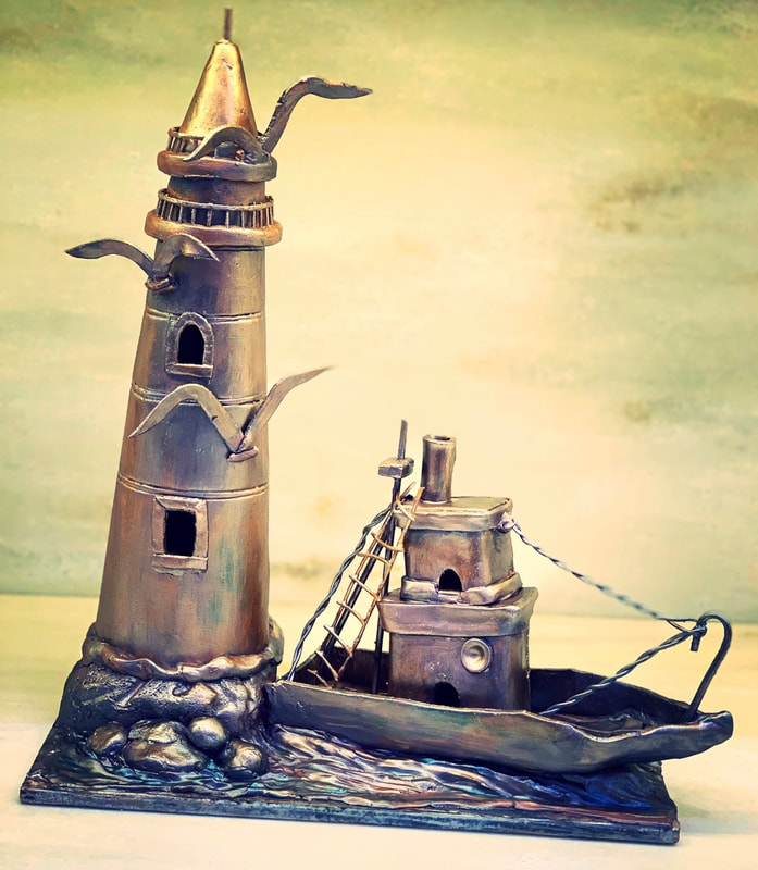 A metallic-styled lighthouse cake sculpture featuring a tall tower with bird accents and a boat with a ladder and smokestack, set on a blue base resembling ocean waves.