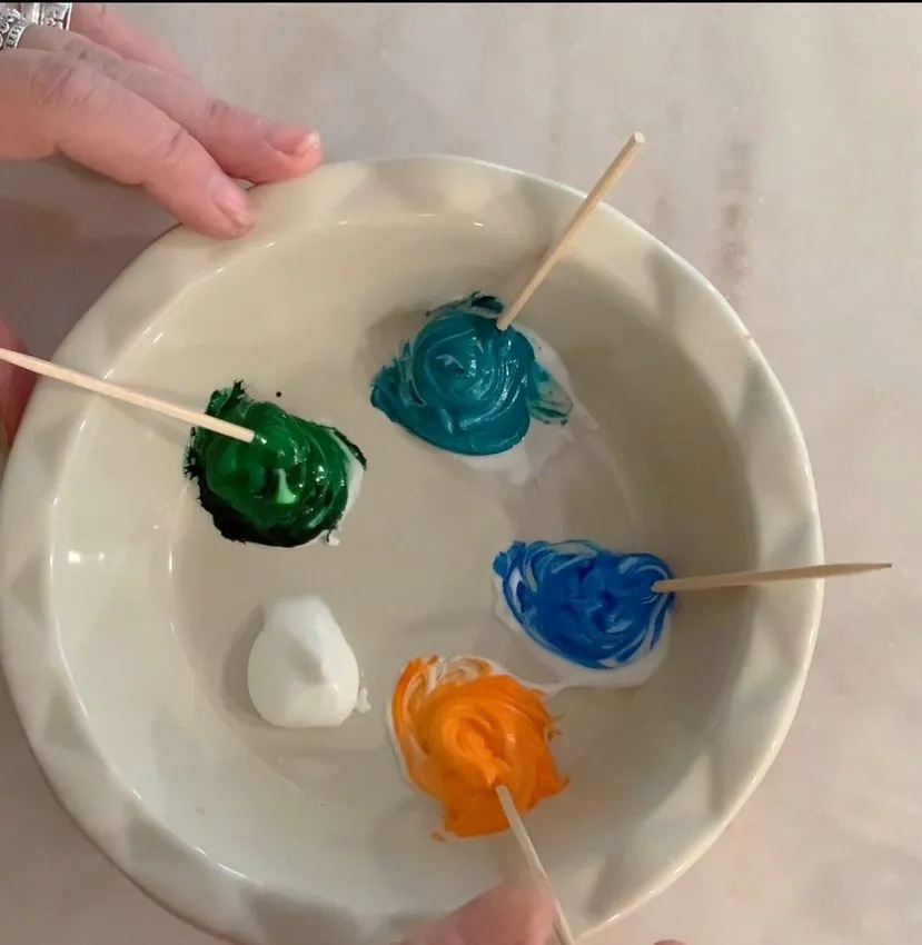 Bowl with white, blue, green, and orange royal icing for decorating.