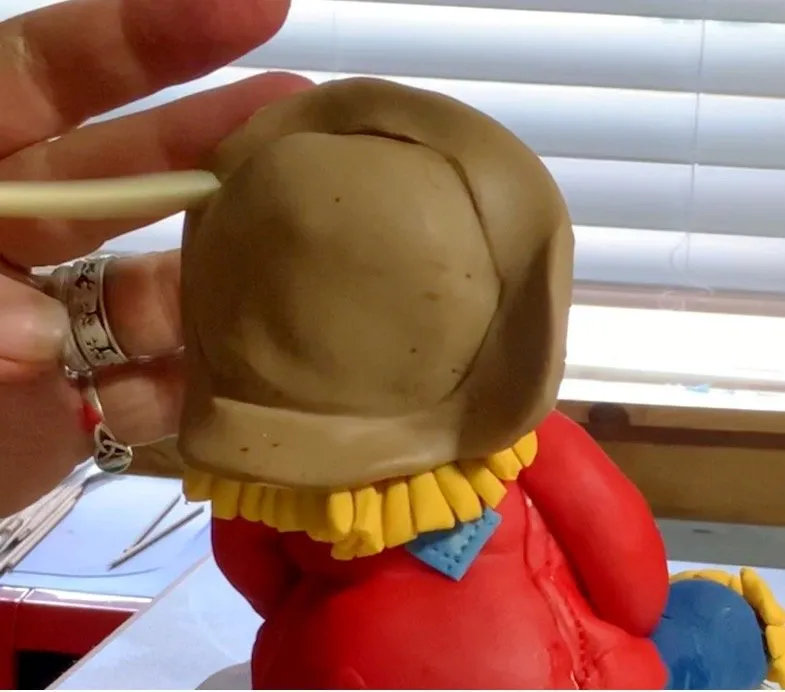 Brown fondant hat being shaped and placed on the scarecrow's head.