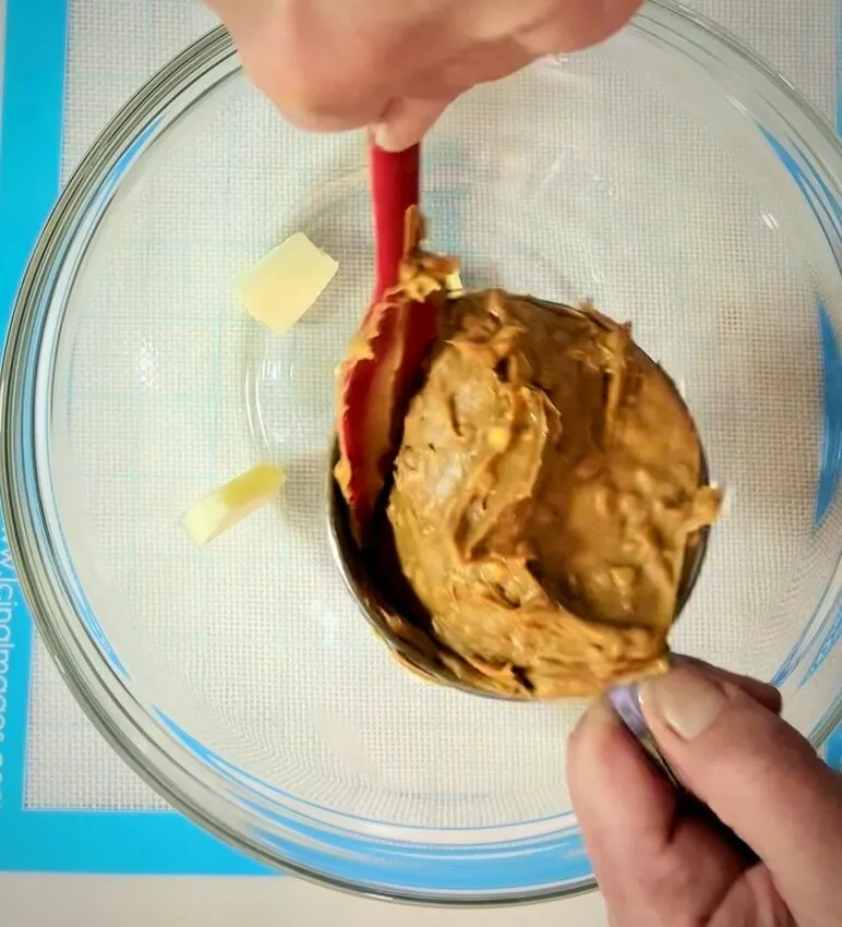 Scraping peanut butter into a bowl with butter.