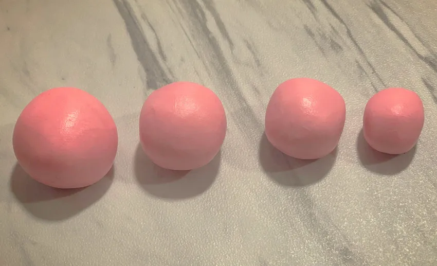Graduated pink modeling chocolate balls for rose petals on a surface.