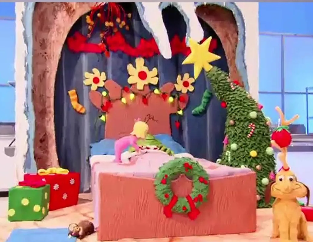 A Grinch-themed bedroom scene cake with a crooked Christmas tree and wrapped gifts.