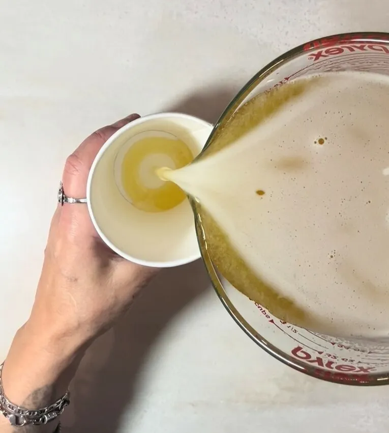 A hand pours the melted gelatin mixture into a large paper cup.