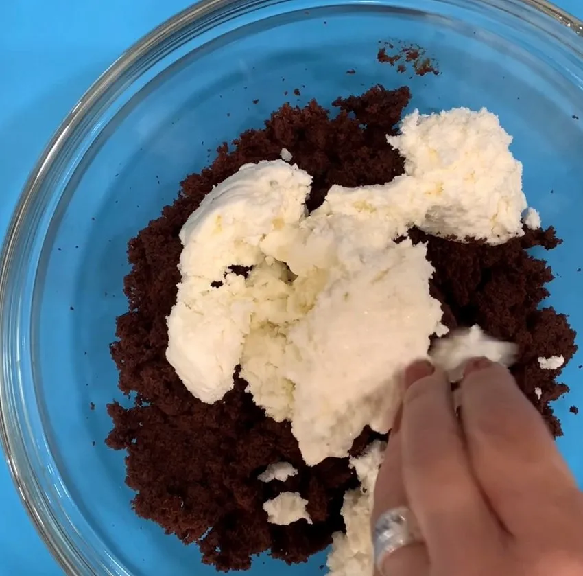 Hand mixing buttercream with cake crumbs in a bowl.