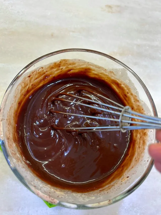 Smooth, glossy chocolate ganache being whisked in a glass bowl