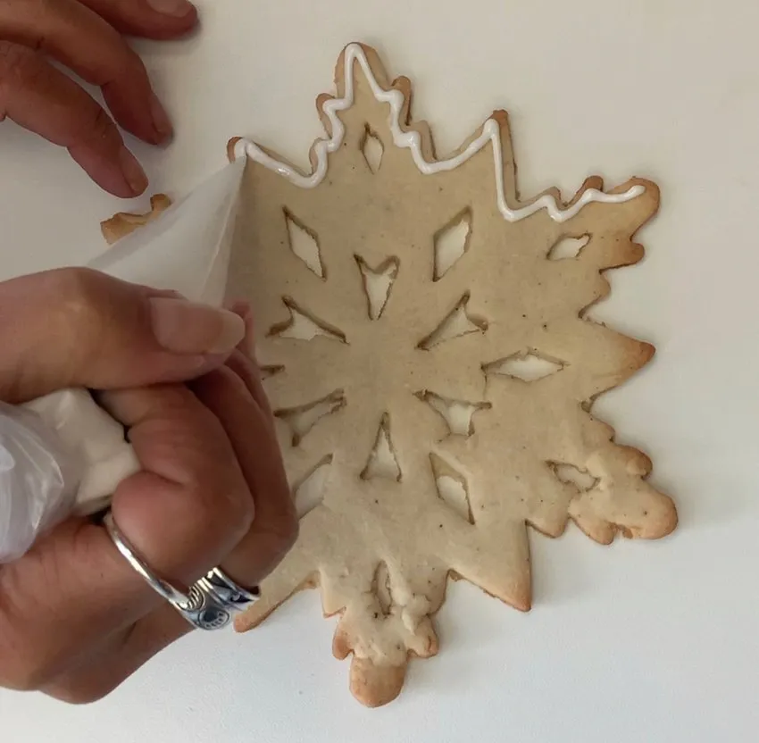 Piping white icing outline on a snowflake-shaped cookie