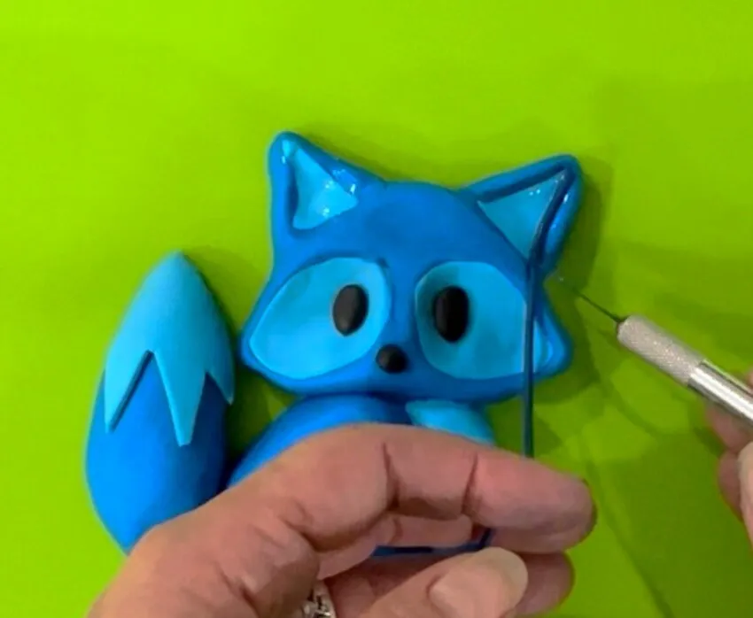 Hands using a tool to outline the fox's ears and eyes with darker fondant.