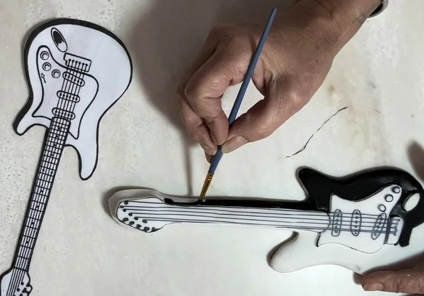 Hand painting details on a fondant-covered guitar cookie with a brush.