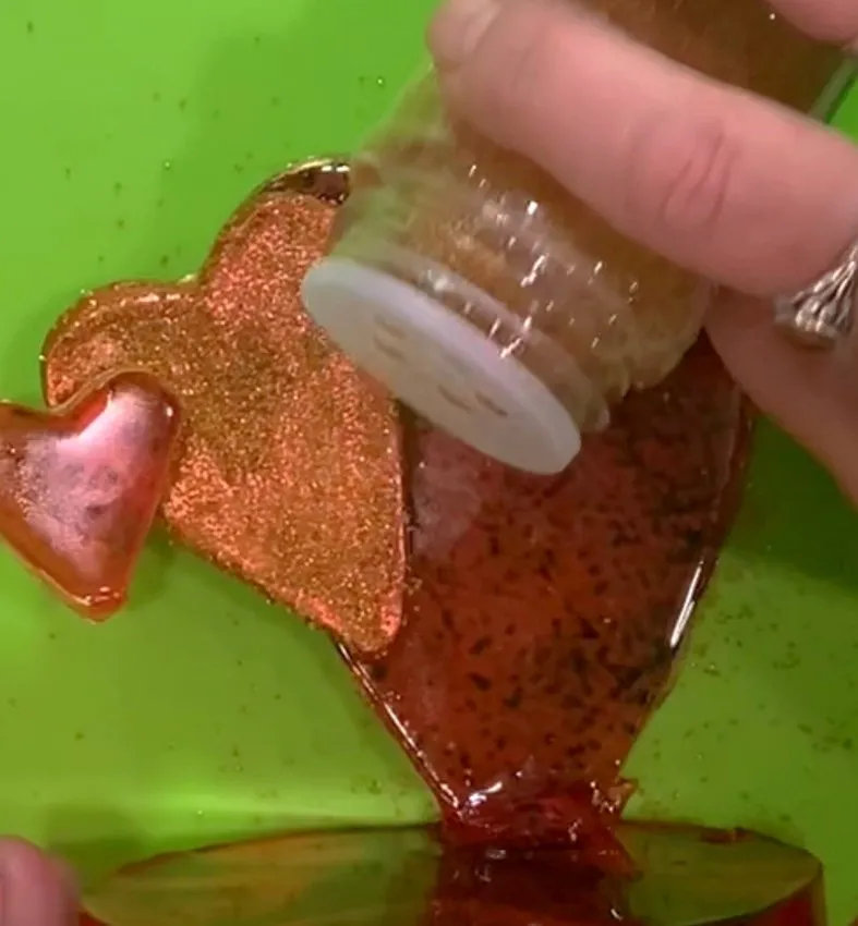 Gold glitter being sprinkled onto a painted isomalt heart piece.