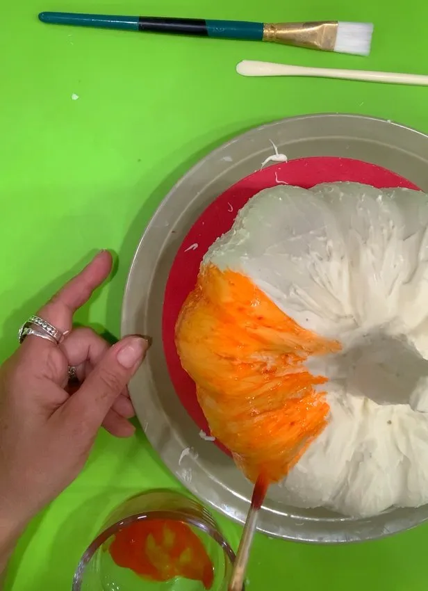 Painting the chocolate pumpkin with orange edible color using a paintbrush.